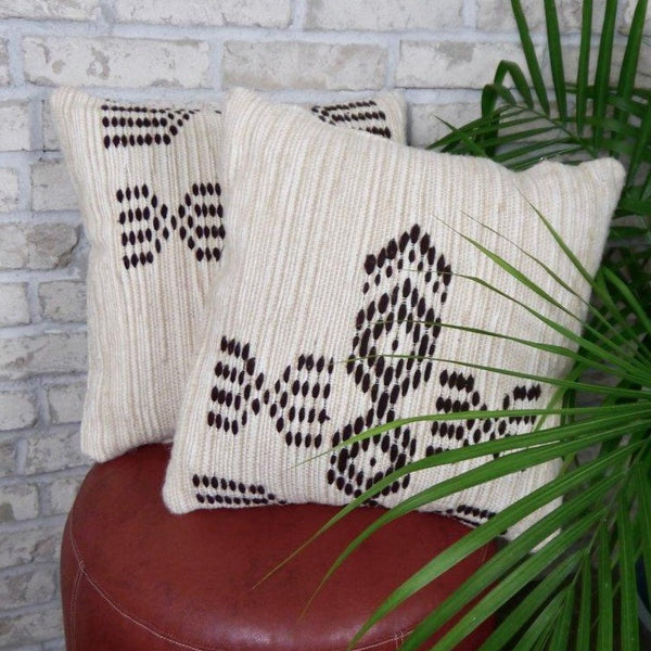 Two patterned pillows on a leather stool near a plant