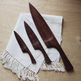 Three wooden kitchen knives in different sizes on a cotton napkin