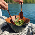 A person tossing salad in a mahogany bowl