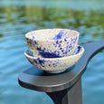 Two hand-painted white and blue bowls on an armchair near a lake