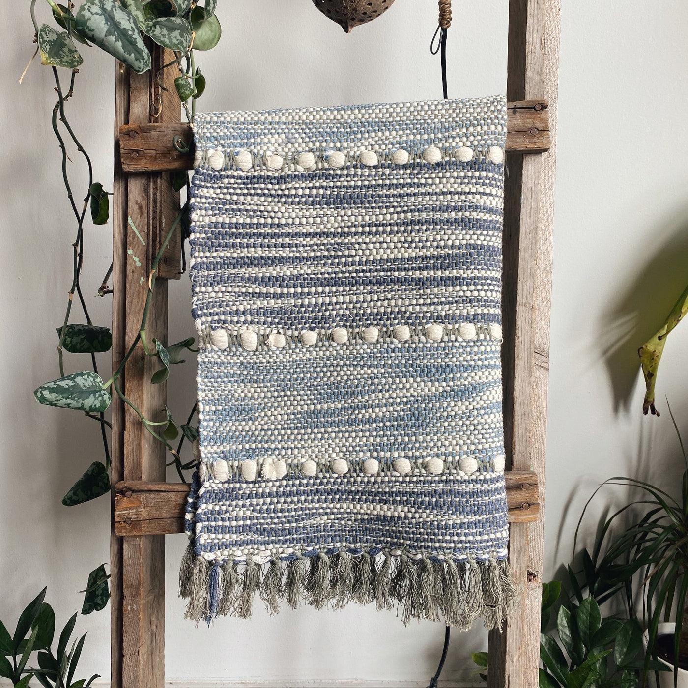 Striped handwoven blue and white cotton rug hanging on a wooden ladder