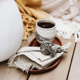 Close up of a wooden serving plate with a coffee mug, fabric napkin and tassel napkin ring  