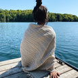 Woman wrapped in a textured blanket onlooking a lake