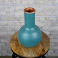 Teal cylinder vase with copper accents on a wooden stool